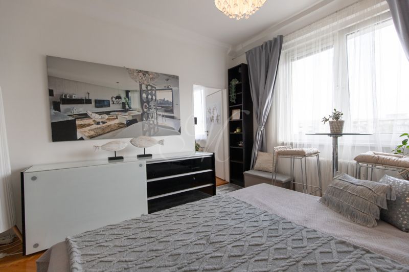 Bedroom in a 2-room apartment with decorative pillows, a painting, and a large window.