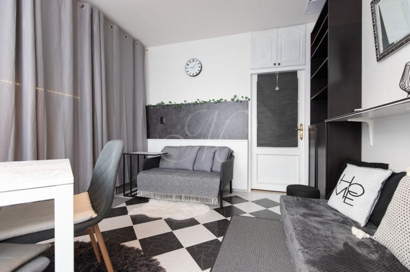 Living room in a 2-room apartment with gray curtains, black and white flooring, and a comfortable couch.