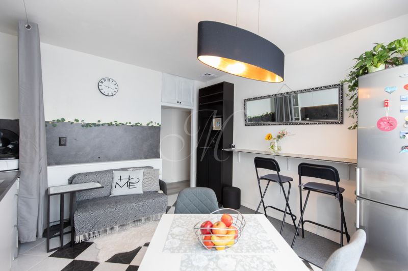 A kitchen in a 2-room apartment with a dining table, bar, refrigerator, and black light fixture.
