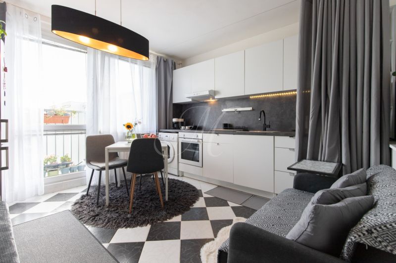 A kitchen in a 2-room apartment with a dining table, curtains, and black and white tiles.