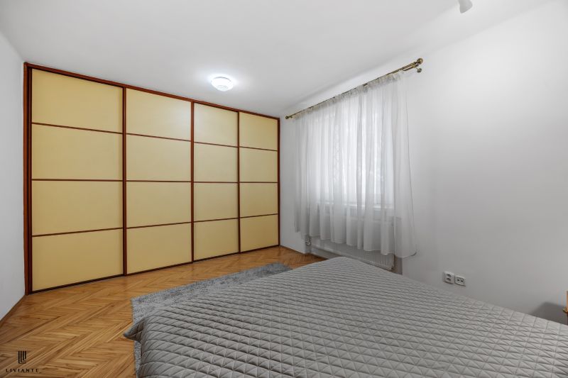 Bedroom in a 2-room apartment with wood-patterned flooring, a wardrobe, and curtains.