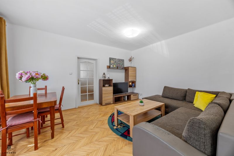 A bright living room in a two-room apartment with a wooden-patterned floor and a comfortable sofa.