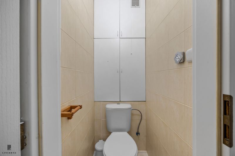 A bathroom with tiles and a white shelf in a 2-room apartment.