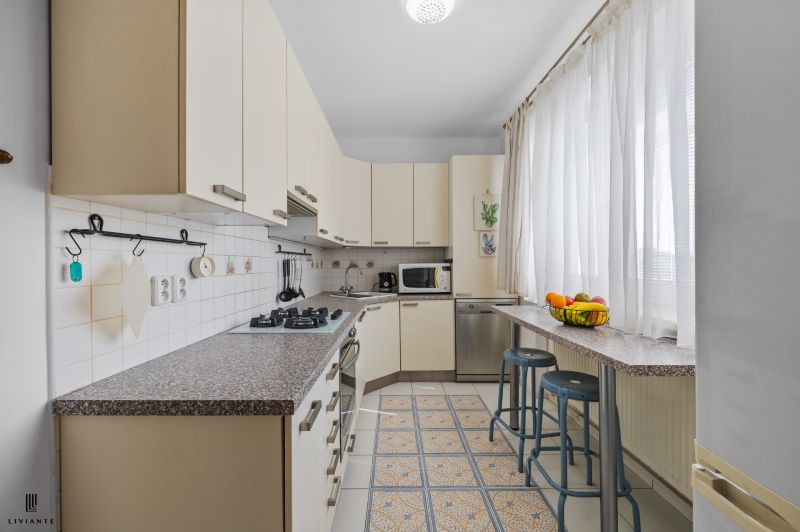 A kitchen in a 2-room apartment with a counter, chairs, and appliances, in light shades.