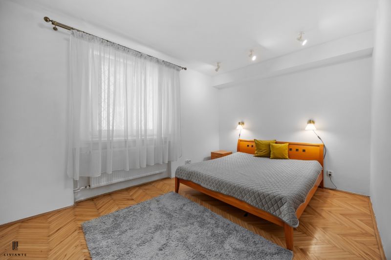 Bedroom with a bed, gray carpet, colorful pillows, wooden decor flooring in a 2-room apartment.