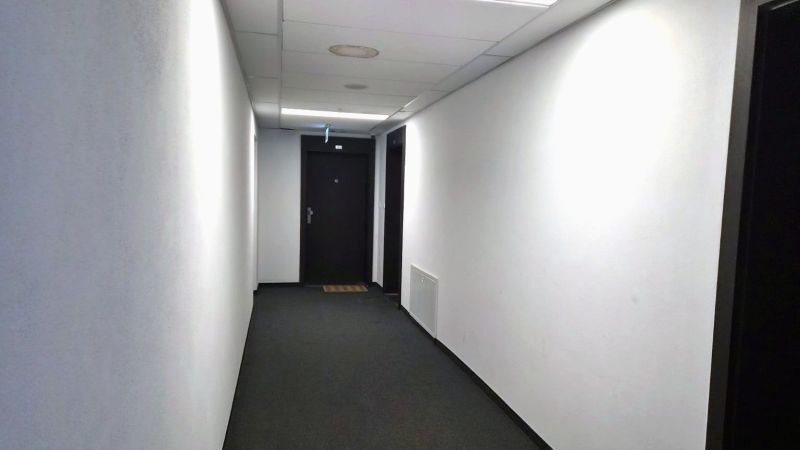 A hallway with white walls and a gray carpet leading to a door.