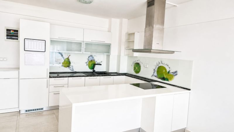 A kitchen in a 2-room apartment with white furniture and glass tiles.