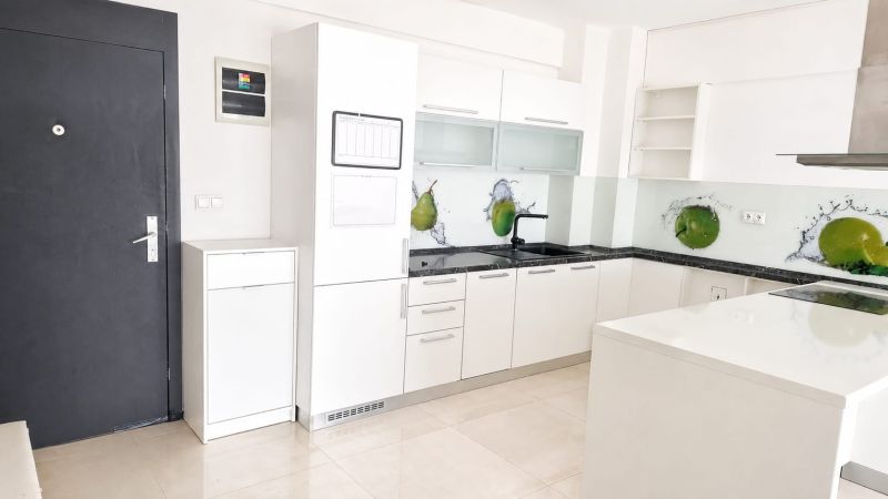 Seamless kitchen in a 2-room apartment with white cabinets and green fruit decor.