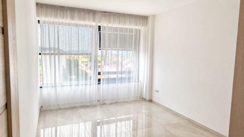 An empty room in a 2-room apartment with white curtains and tiled flooring.