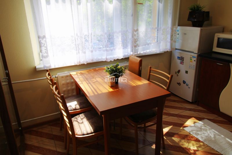 Dining area with a wooden table and chairs in a studio apartment with a view of greenery.