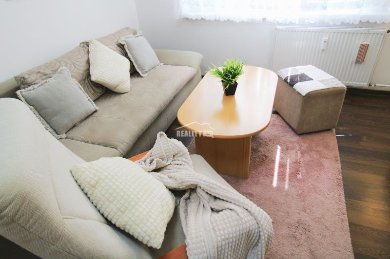 Living area of a studio apartment with a comfortable sofa and a table on a floor with a wooden decor.