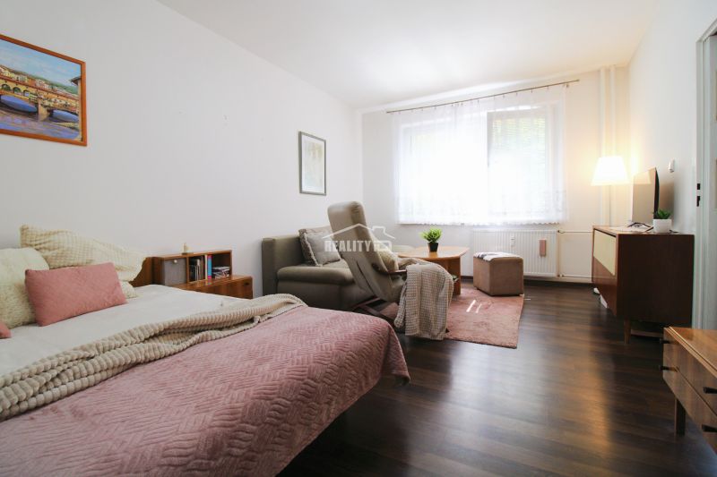 Interior of a 1-room apartment with a bed, an armchair, and a wooden decor floor.