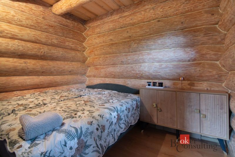 A bedroom in a family house with wooden walls, a patterned bed, and a cabinet.