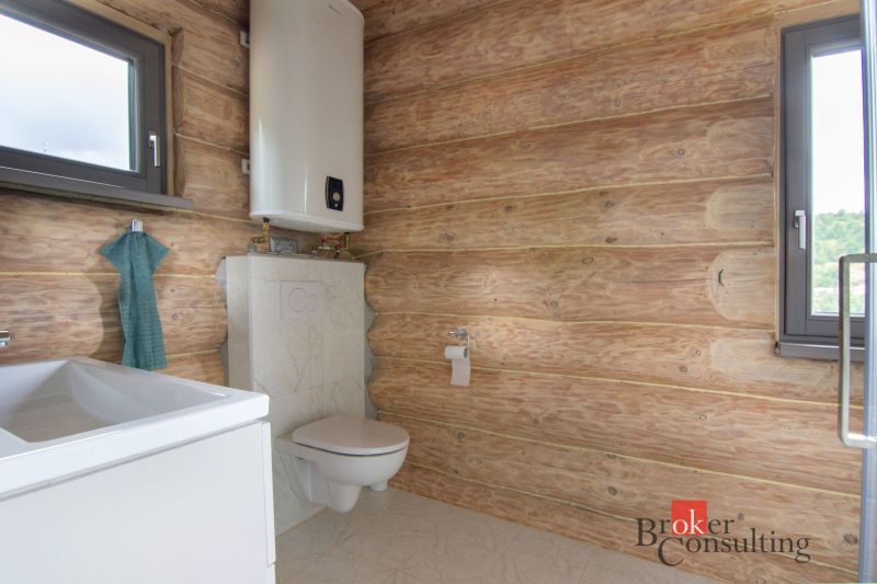 A bathroom with wooden walls, a sink, a toilet, and a boiler in a family house.