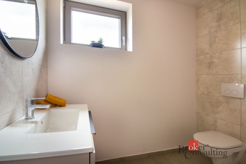 A bathroom in a family house with light tiles, a sink, and a toilet.