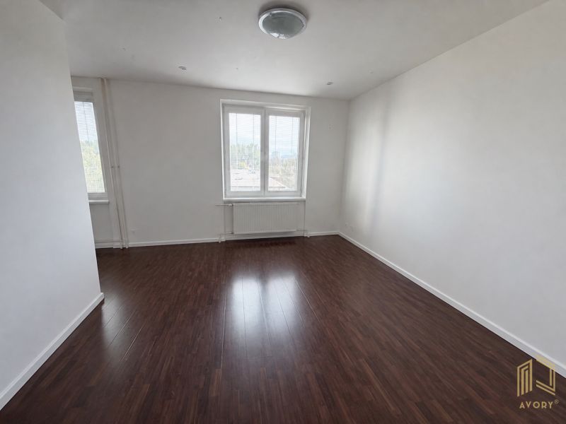 A bright room in a 2-room apartment with a wooden decor floor, one window with a radiator.