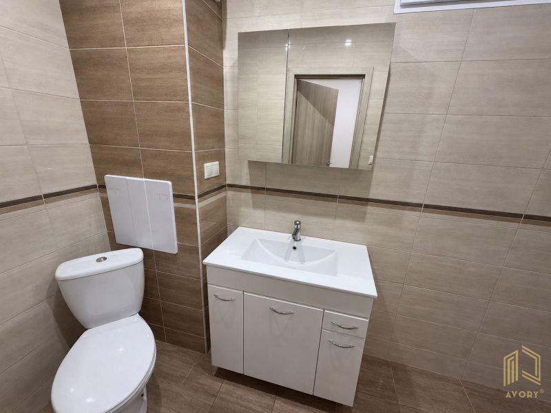 Bathroom with a sink, mirror, and toilet in a 2-room apartment, with ceramic tiles.