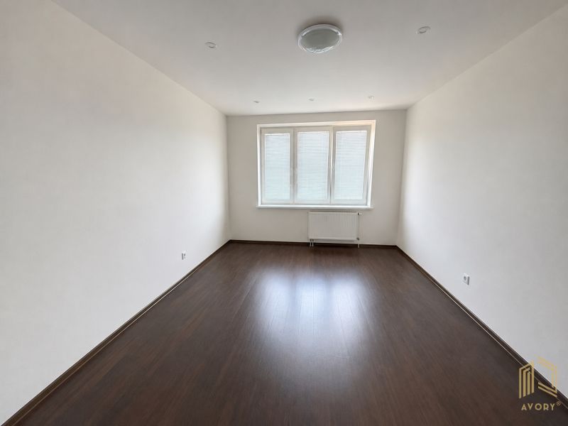 A room in a 2-room apartment with a wooden decor floor and three windows.