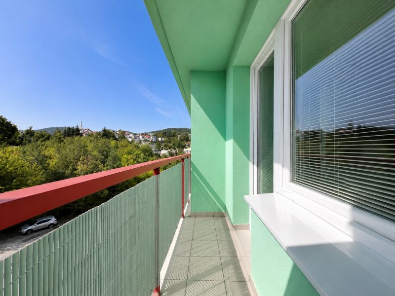 A balcony in a one-room apartment with a view of greenery and a blue sky.