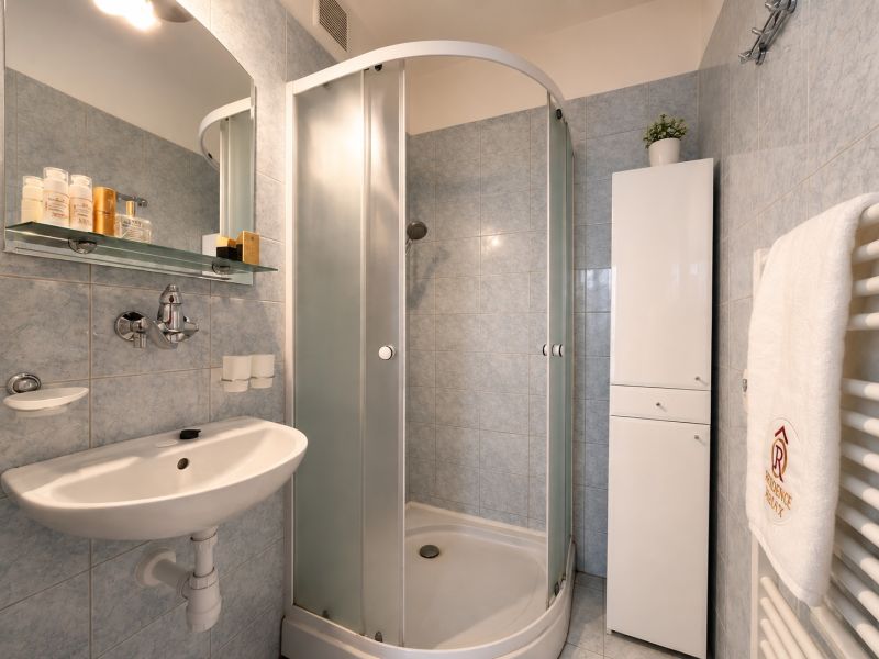 A bathroom in a studio apartment with a corner shower and a modern sink.