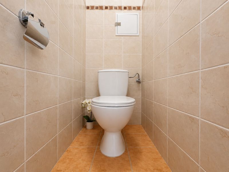 Toilet in the bathroom with cream tiles in a studio apartment.
