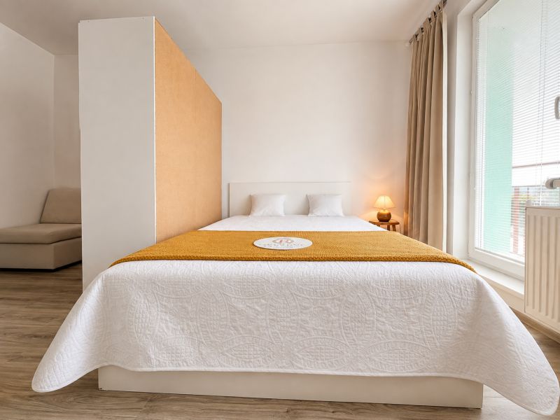 A bedroom in a studio apartment with a wood-patterned floor, a bed, and curtains.