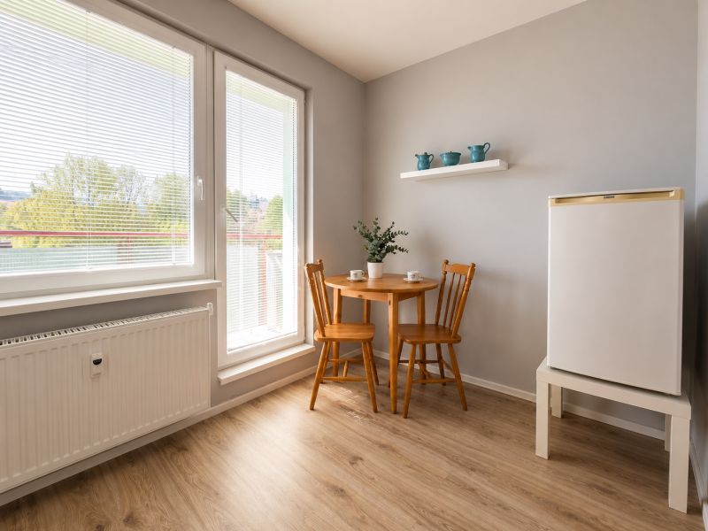 Dining area in a studio apartment with wood-patterned flooring and balcony doors.