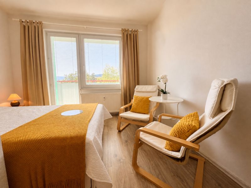 A room in a one-bedroom apartment with light furniture and a wood-patterned floor.