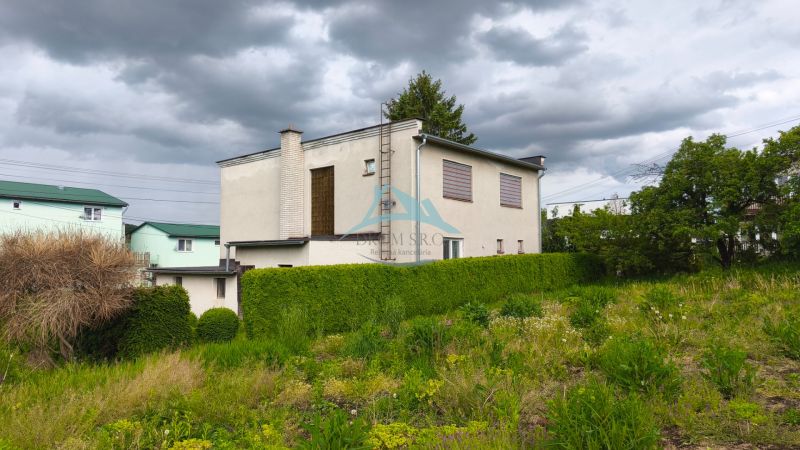 A family house in Nenince surrounded by greenery and a hedge under a cloudy sky.