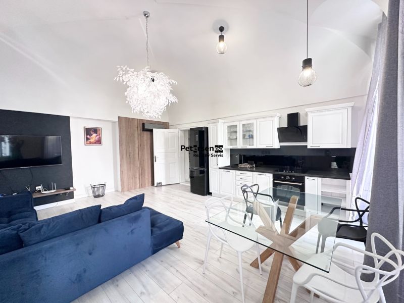 Living room in a three-room apartment with a sofa, kitchen unit, and glass table.