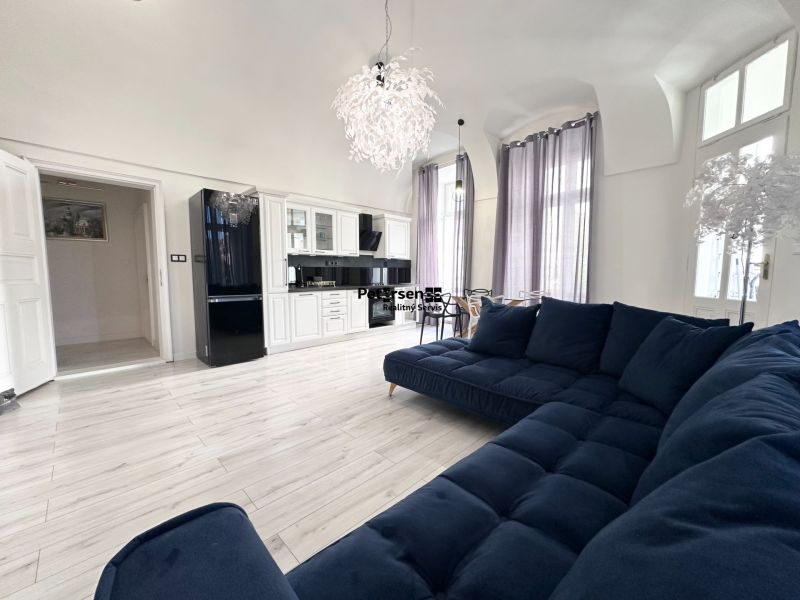 Living room with a dark blue couch, kitchen, and wooden decor flooring in a 3-room apartment.