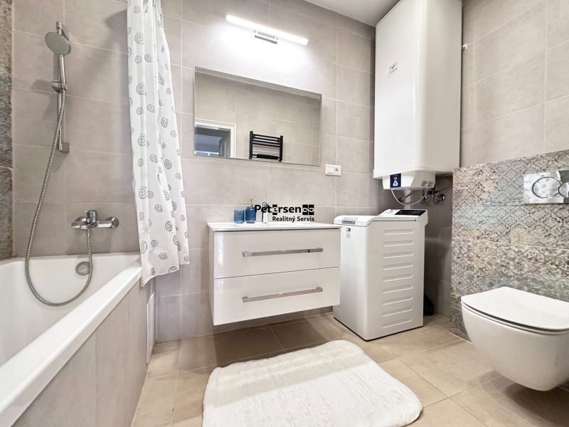 A bathroom in a 3-room apartment with a bathtub, washing machine, and a large mirror.