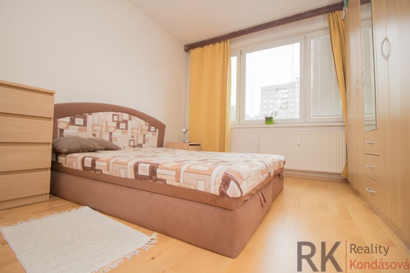 A bright bedroom with a bed, wooden floor decor, and yellow curtains in a three-room apartment.