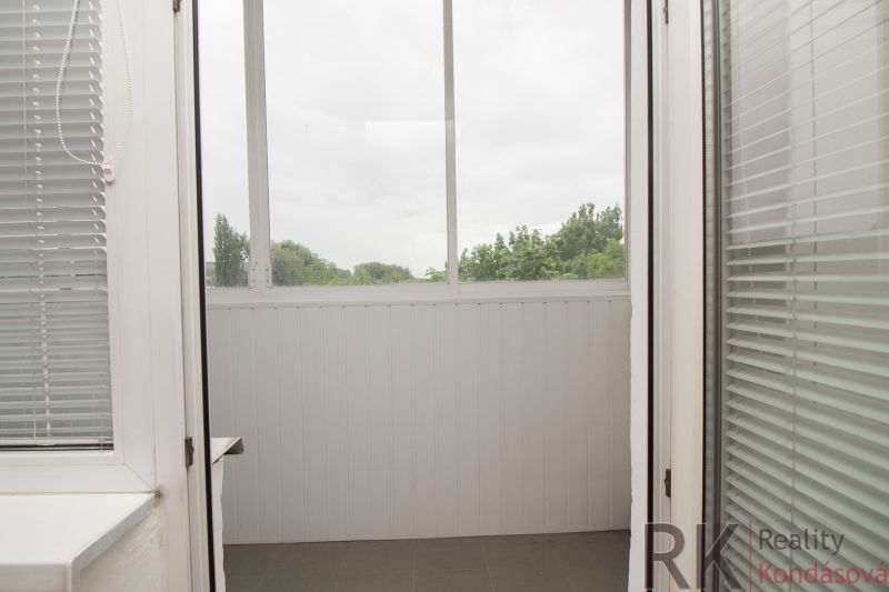 A bright loggia with blinds in a 3-room apartment with a view of greenery.
