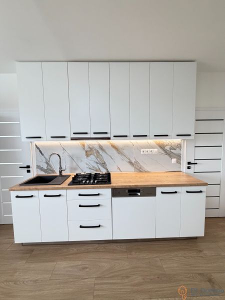 Kitchen unit in a one-room apartment with white cabinets and a wooden decor floor.