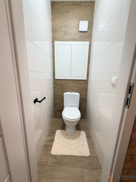 Bathroom with toilet, white tiles, and a floor with a wood decor in a studio apartment.