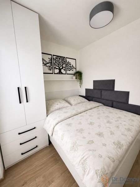 A bedroom in a studio apartment with a built-in wardrobe, a bed, and a wooden decor floor.