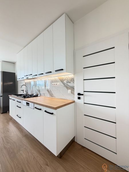 A kitchen in a studio apartment with white cabinets, marble tiles, and a wood-patterned floor.