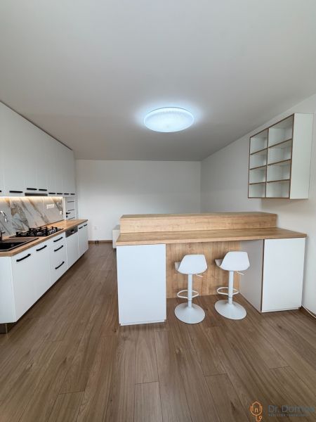 A kitchen in a studio apartment with a wood-patterned floor, white furniture, bar stools.