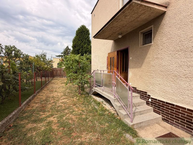 A family house in Nové Zámky with a garden, stairs, and a fence, surrounded by greenery.