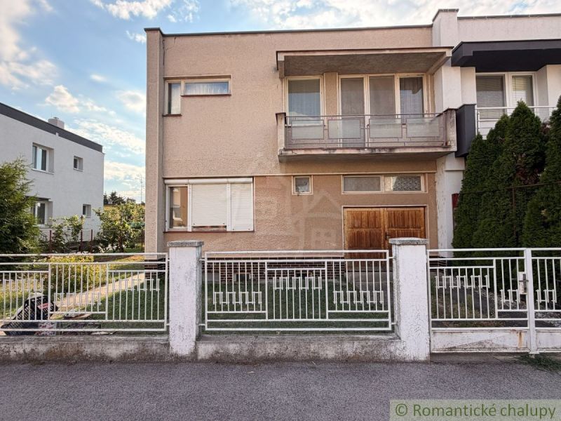 A family house in Nové Zámky with a balcony and a garden, enclosed by a white fence.