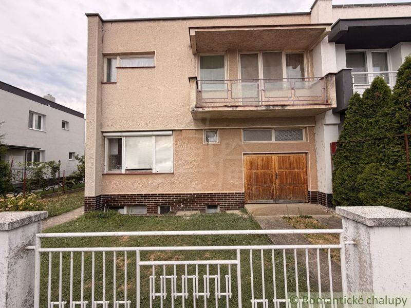 A family house in Nové Zámky with an old garage and a balcony, enclosed by a metal fence.
