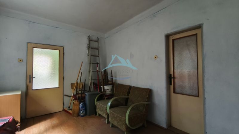 A room in a family house with armchairs, a ladder, and brooms on a wooden-decorated floor.