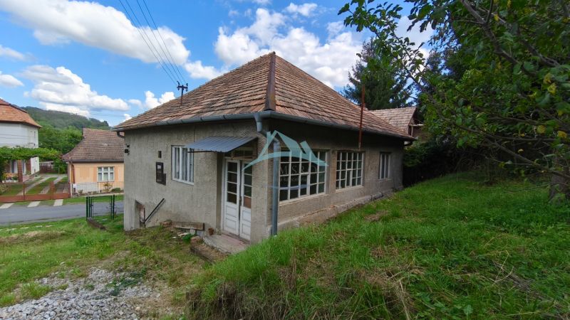 A family house in Olováry with a sloped roof, surrounded by a garden and green trees.