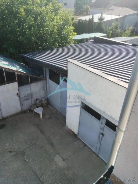 A family house in Nitra with a garage, a concrete yard, and greenery in the background.