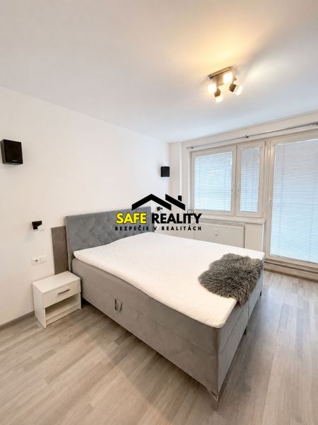 A bedroom with a double bed, wooden decor flooring, and a window in a three-room apartment.