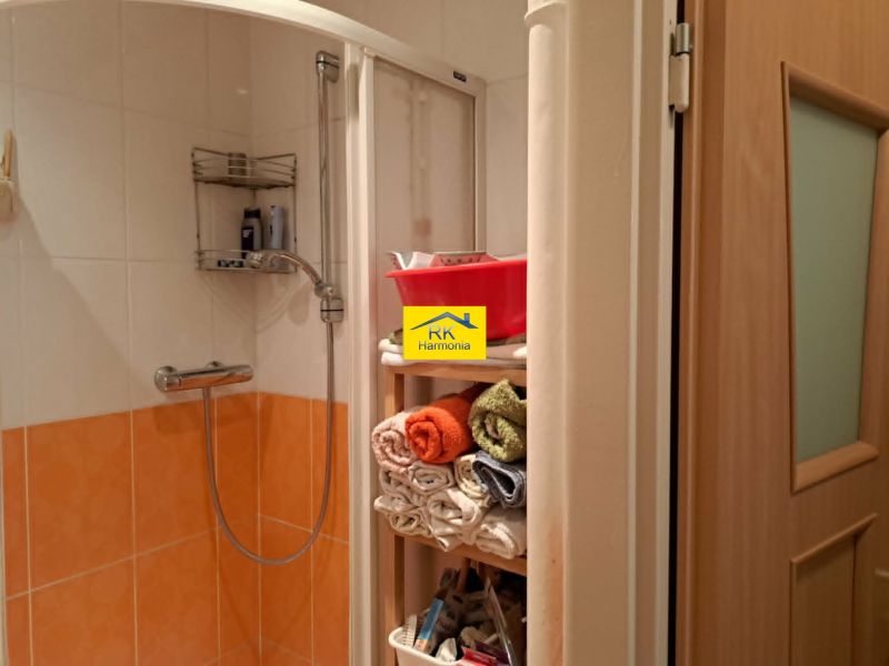 Shower corner with orange tiles and a shelf with towels in a 2-room apartment.