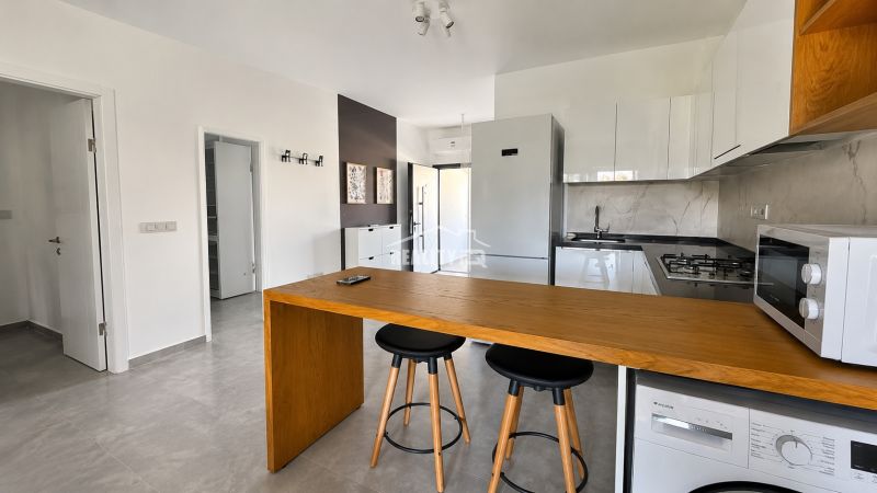 A kitchen in a studio apartment with a bar counter, white kitchen cabinets, and appliances.