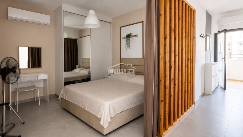 Studio apartment with a bed, mirrored wardrobe, desk, and access to a balcony.