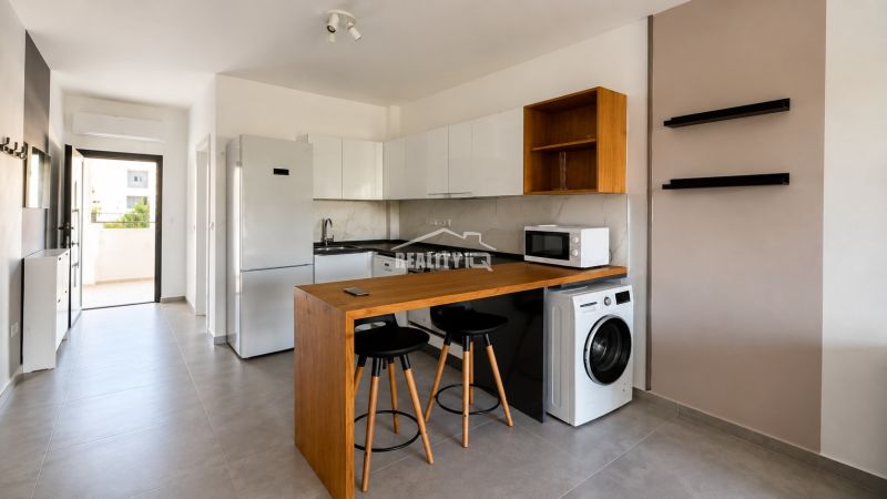 A kitchenette in a studio apartment with a bar counter, washing machine, and refrigerator.